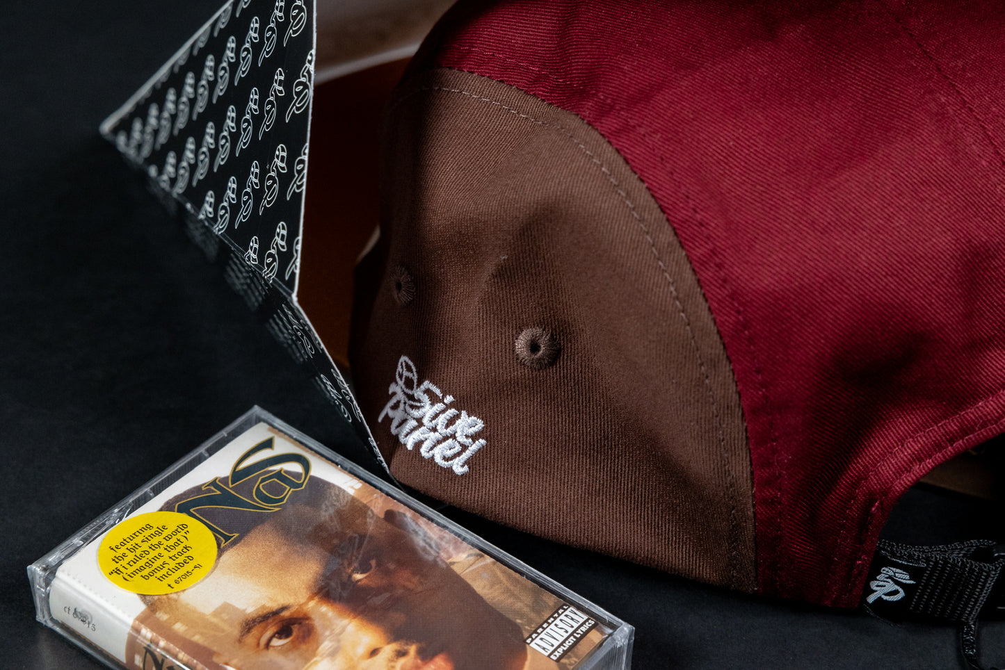 "imagine that" 5ive Panel Hat, packaging box and cassette, black background.