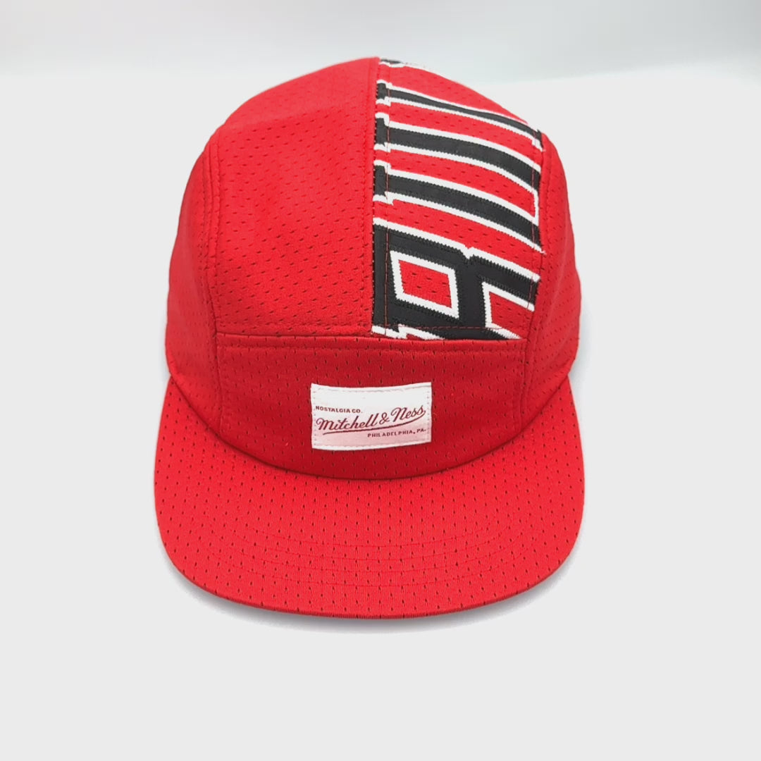 Spinning red and white upcycled MJ jersey made into a 5 Panel Hat, BULLS stitched on the top panel, white background.