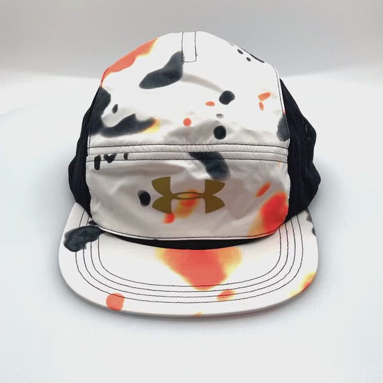 Spinning orange, white, black Under Armour 5 Panel Hat, gold logo on the front, with a white background.