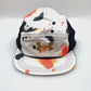 Spinning orange, white, black Under Armour 5 Panel Hat, gold logo on the front, with a white background.