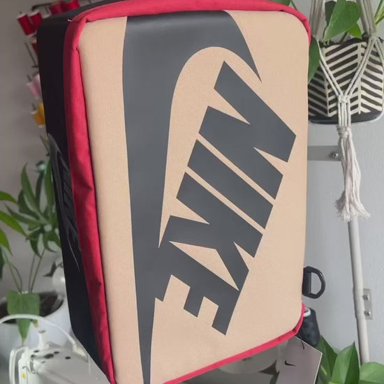 The making of a black and tan NIKE shoe box bag upcycled to a 5 Panel Hat, zipper on right side panel, with white background.