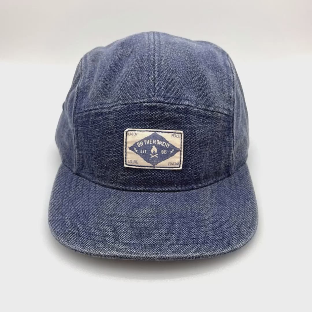 Spinning Blue denim Clakllie 5 Panel Hat with "On The Moment" logo on the front panel.