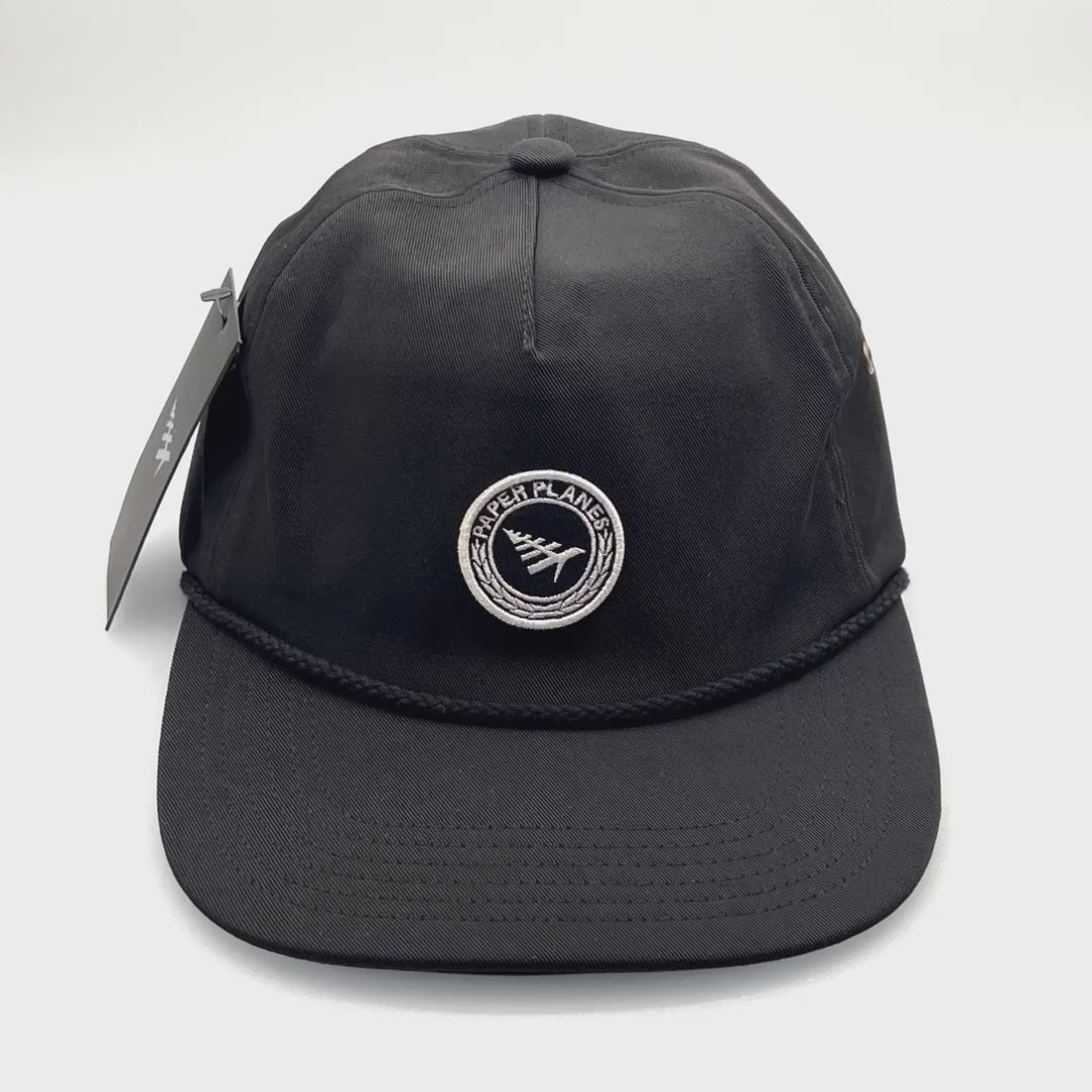 Spinning black polyester Paper Planes 5 Panel Hat, embroidered logo on the front, with a white background.