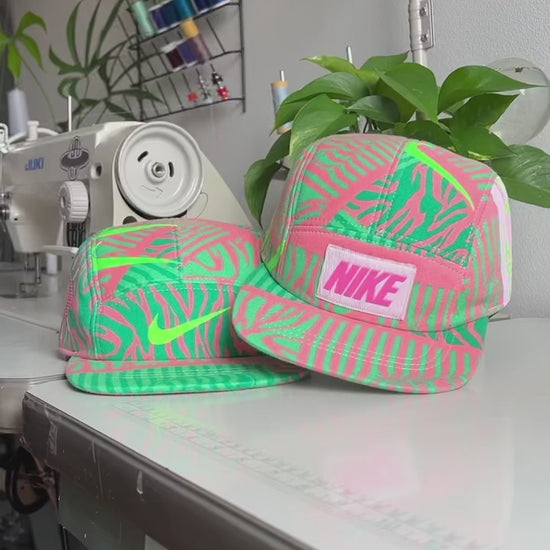 The making of a fluorescent green and pink Nike sweatshirt fleece upcycled into a 5 Panel Hat, Nike logos throughout, with a white background.