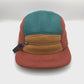 Spinning brown, tan and cyan Patagonia fleece 5 Panel Hat upcycled, zipper on the front, with a white background.