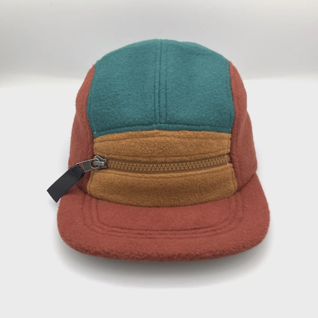 Spinning brown, tan and cyan Patagonia fleece 5 Panel Hat upcycled, zipper on the front, with a white background.