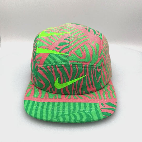 Spinning fluorescent green and pink Nike sweatshirt fleece upcycled into a 5 Panel Hat, Nike logos throughout, with a white background.