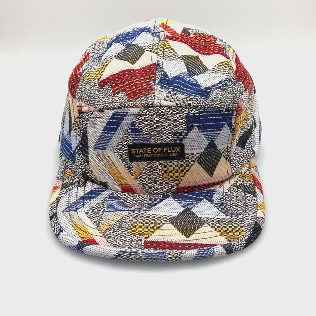 Spinning grey and black Staple Standard Pigeon 5 Panel Hat, with a white background.