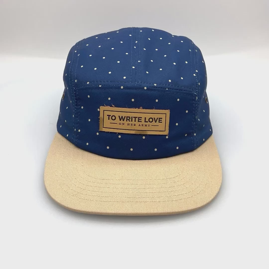Spinning tan and navy polka dots TWLOHA 5 Panel Hat, leather logo on the front, with a white background.