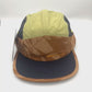 Spinning nylon navy, brown, and olive Paper Planes 5 Panel Hat, orange Paper Planes logo on the front, with a white background.
