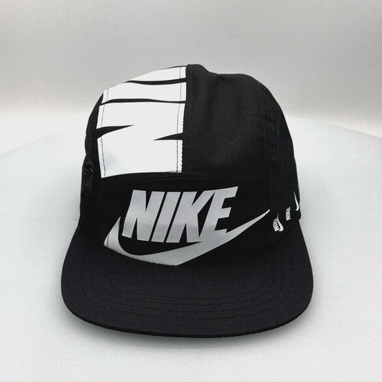 Spinning black and white NIKE shoe box bag upcycled to a 5 Panel Hat, zipper on right side panel, with white background.