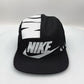 Spinning black and white NIKE shoe box bag upcycled to a 5 Panel Hat, zipper on right side panel, with white background.