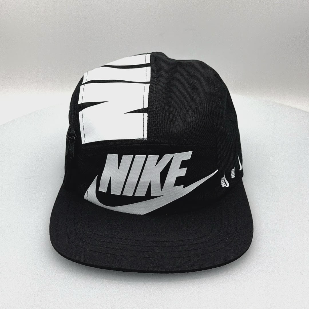 Spinning black and white NIKE shoe box bag upcycled to a 5 Panel Hat, zipper on right side panel, with white background.